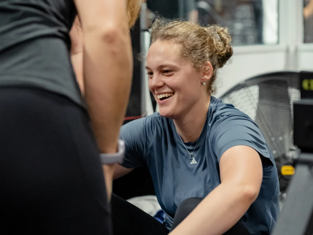 Lachende Teilnehmerin am Rudergerät mit Coach – Wiedereinstieg bei Flensfitness
